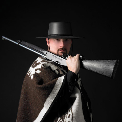 A portrait of Thad Foster in a hat holding a rifle.