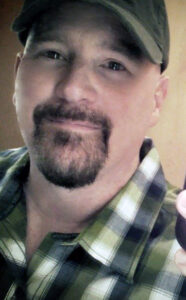 A portrait of Thad Foster in a baseball cap smiling gently.
